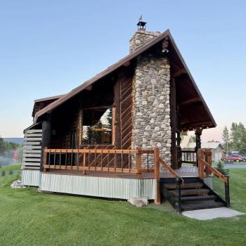 The cabin's exterior is a harmonious mix of natural materials, with large logs and weathered wood giving it an authentic, mountain cabin feel.