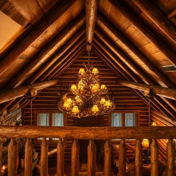 Look up to admire the incredible log craftsmanship and the grand antler-style chandelier, casting a warm, golden glow across the soaring vaulted ceilings.