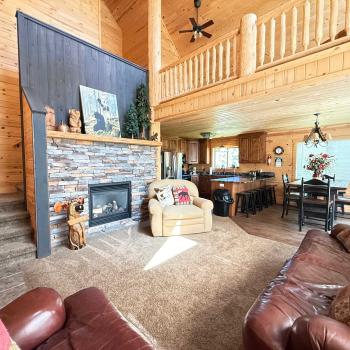 The expansive open-concept main floor features soaring high ceilings, comfortable leather seating, and a grand stone fireplace.