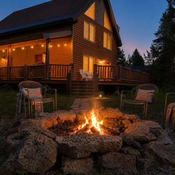 Gather under the stars around the grand stone fire pit, beautifully set against the warm, glowing backdrop of the log cabin and string-lit wrap-around deck.
