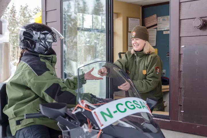 A snowmobiler stops at the West Yellowstone entrance station while a ranger hands over a park map