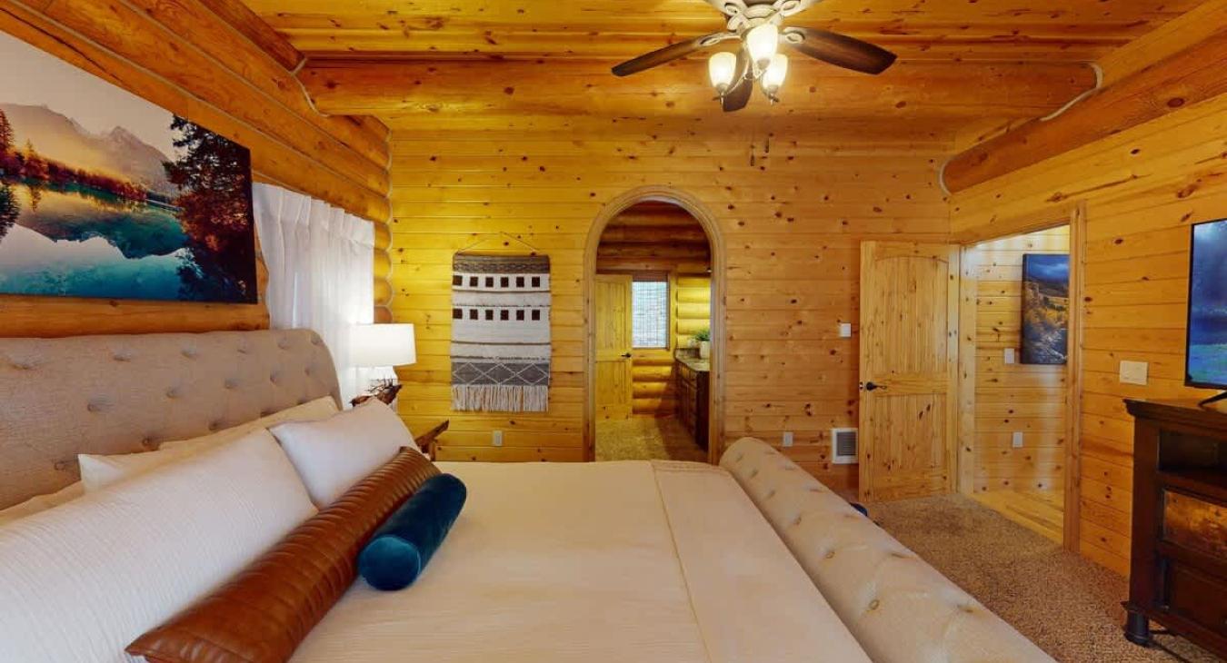 The room’s decor includes subtle touches of luxury, such as an area rug under the bed, a sleek dresser with modern accents, and framed art on the walls that add personality without overwhelming the space.