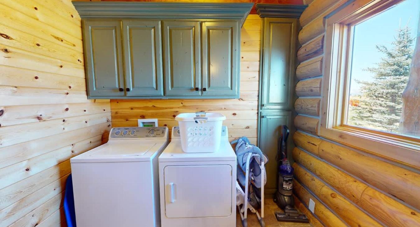 The laundry room in the cabin is a practical yet cozy space that maintains the cabin’s rustic charm. Above the countertop, two wooden cabinets are mounted on the wall, providing ample storage space for laundry essentials.