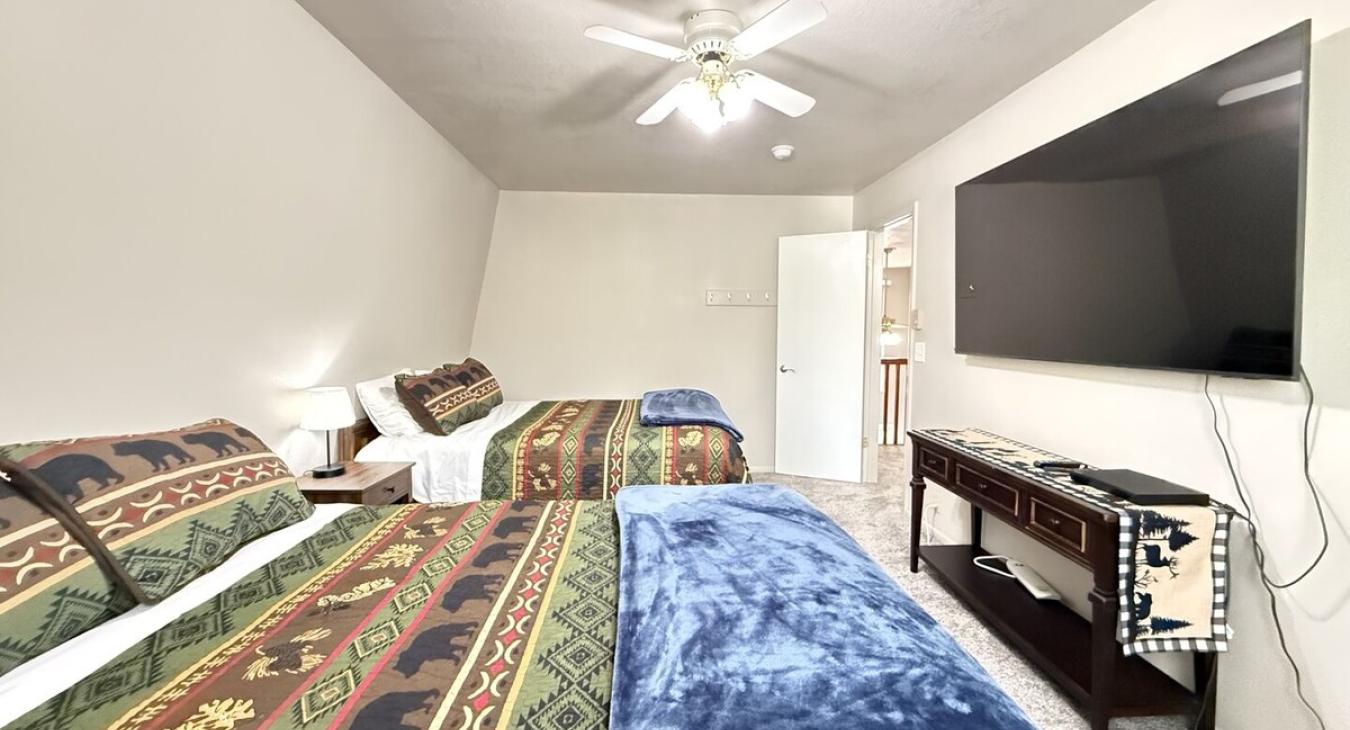 This bedroom features 2 queen beds that can comfortably fit up to 4 guests. It also has a window overlooking the outside of the cabin and a luggage racks for your bags.