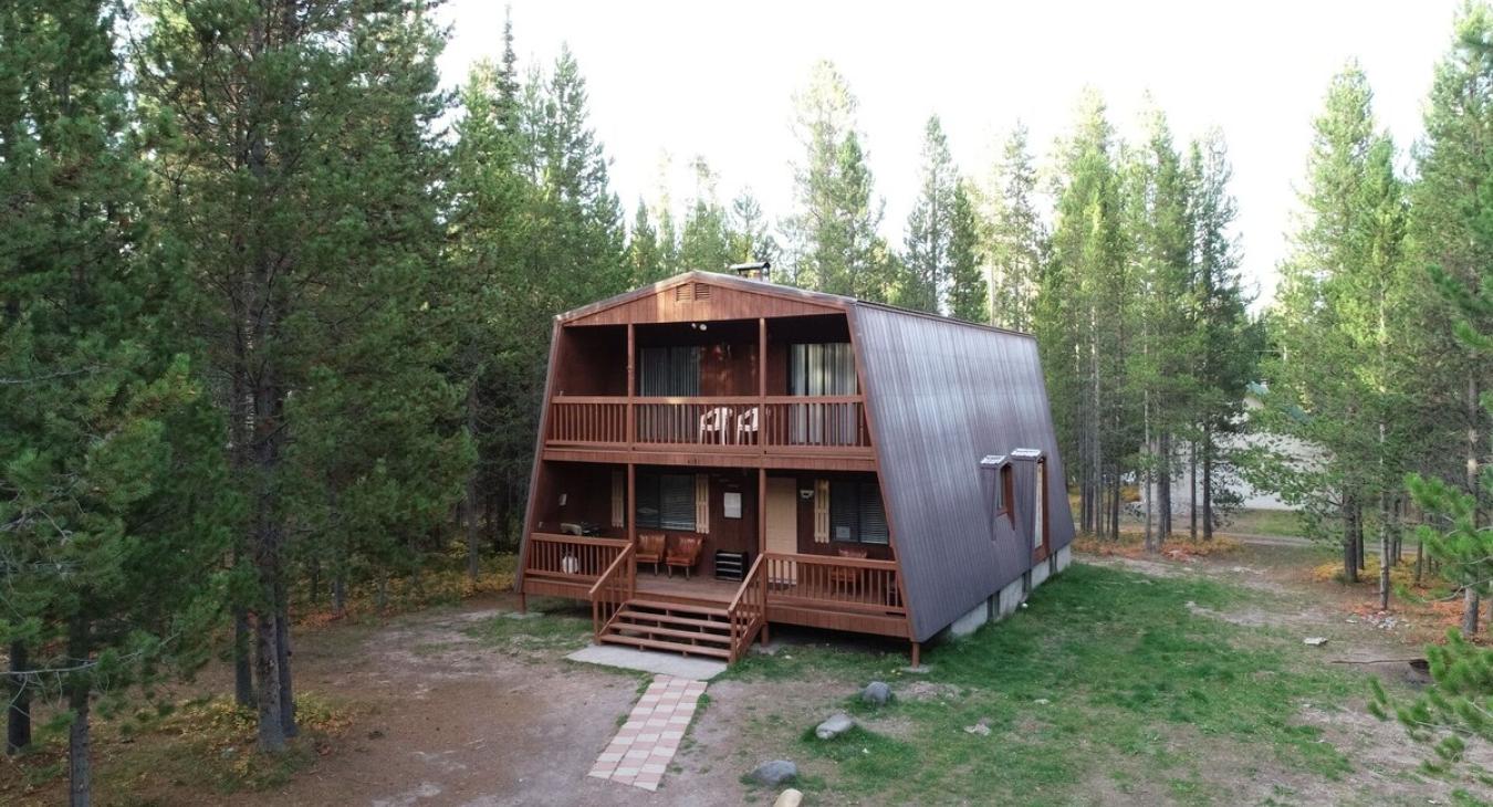 The front of the cabin has a simple, rustic design with lots of wood siding and a small porch. It's also small, with a single entrance. You can also see the surrounding forest from this angle.
