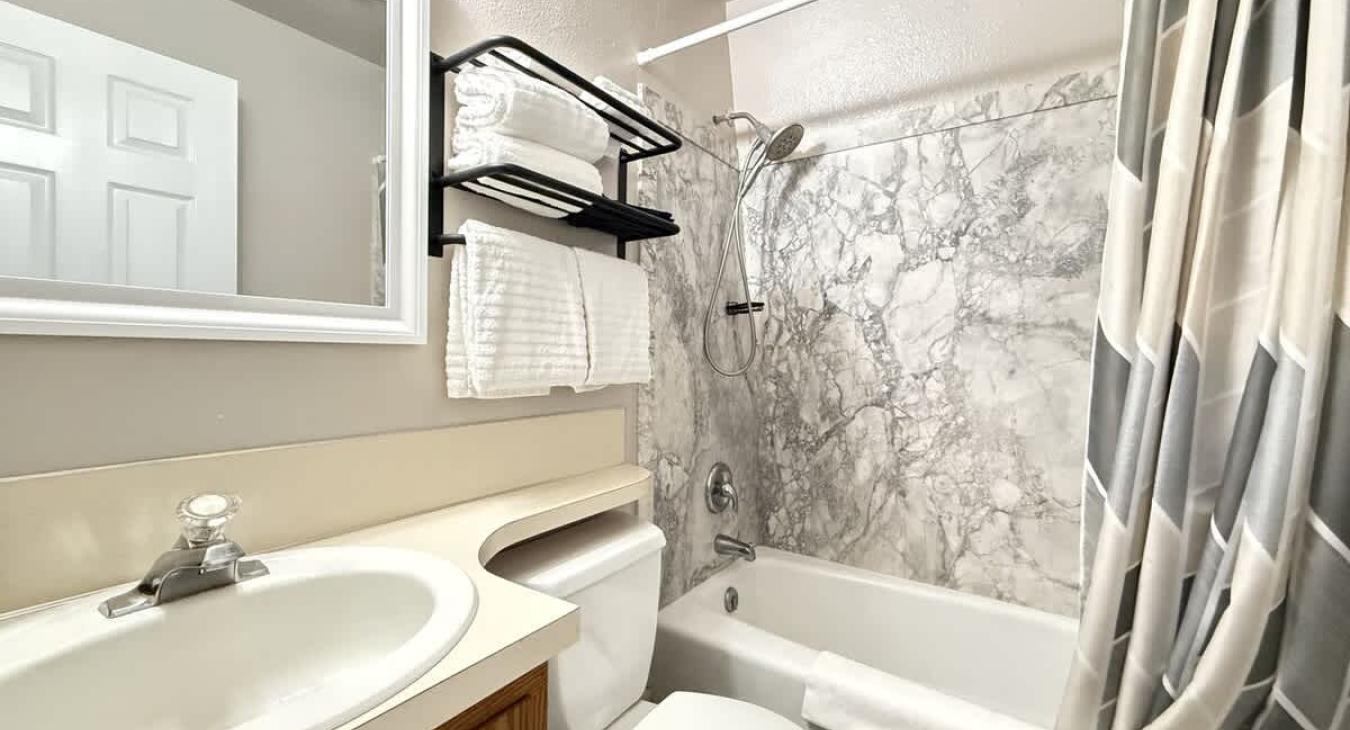 Full common bathroom. Tub and shower combo with shampoo, conditioner, and body wash provided. Toilet and sink vanity with storage underneath.