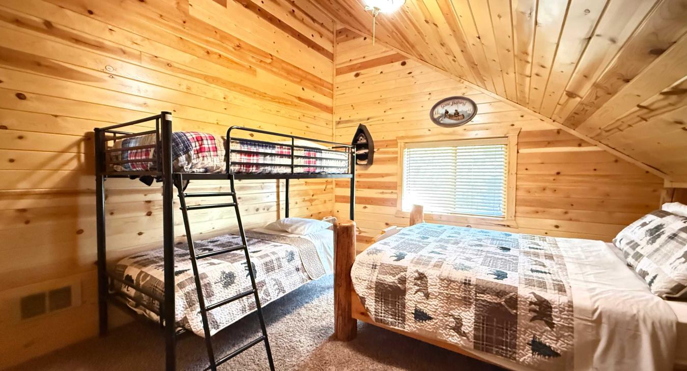 Bright and spacious, this upstairs family room features a clean twin-over-twin bunk bed alongside a matching log-framed bed setup.