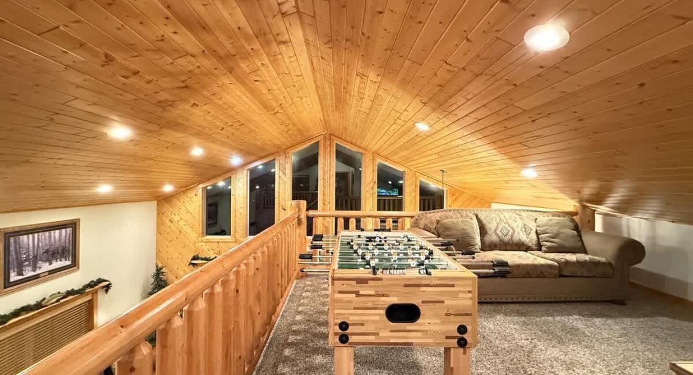 Open to the floor below, the loft overlooks the main living area, with a wooden banister railing made of log posts