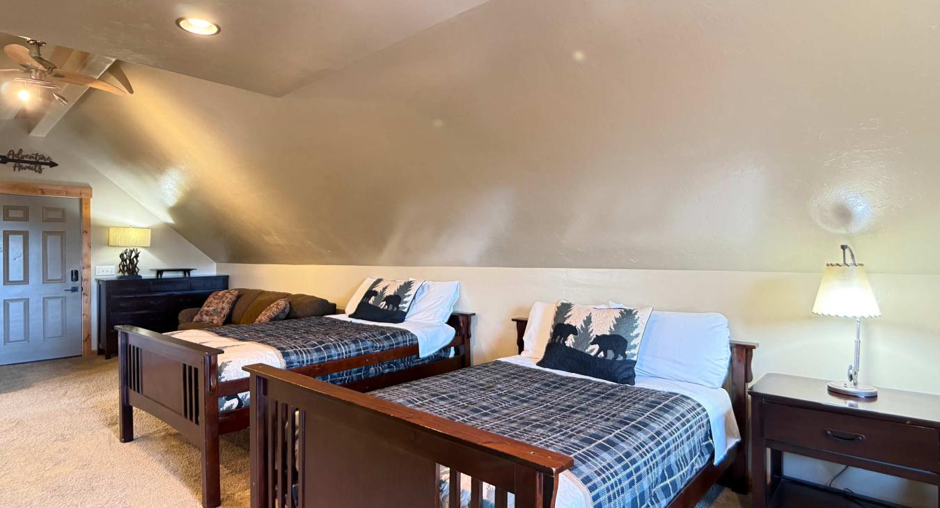 The main sleeping area features two sturdy double beds styled with rustic pine-tree quilts, ideal for a deeply restful night's sleep.