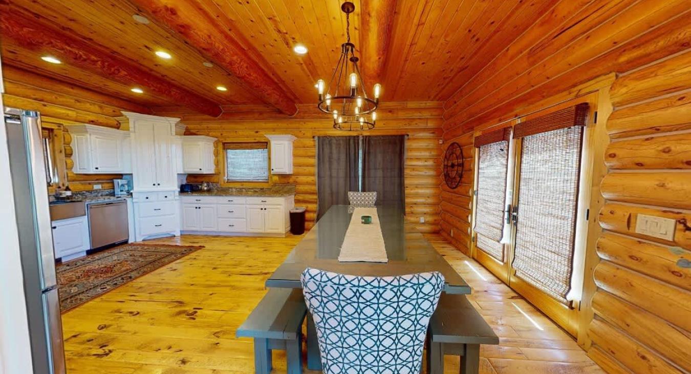 Imagine stepping into a warm and inviting dining room in a cabin, where rustic elegance takes center stage. The room is centered around a long, sturdy wooden dining table that stretches across the space. The table is large enough to seat everyone.