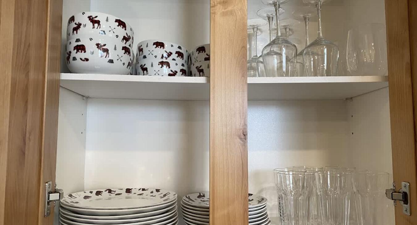 Kitchen is equipped with cups, wine glasses, and plates.