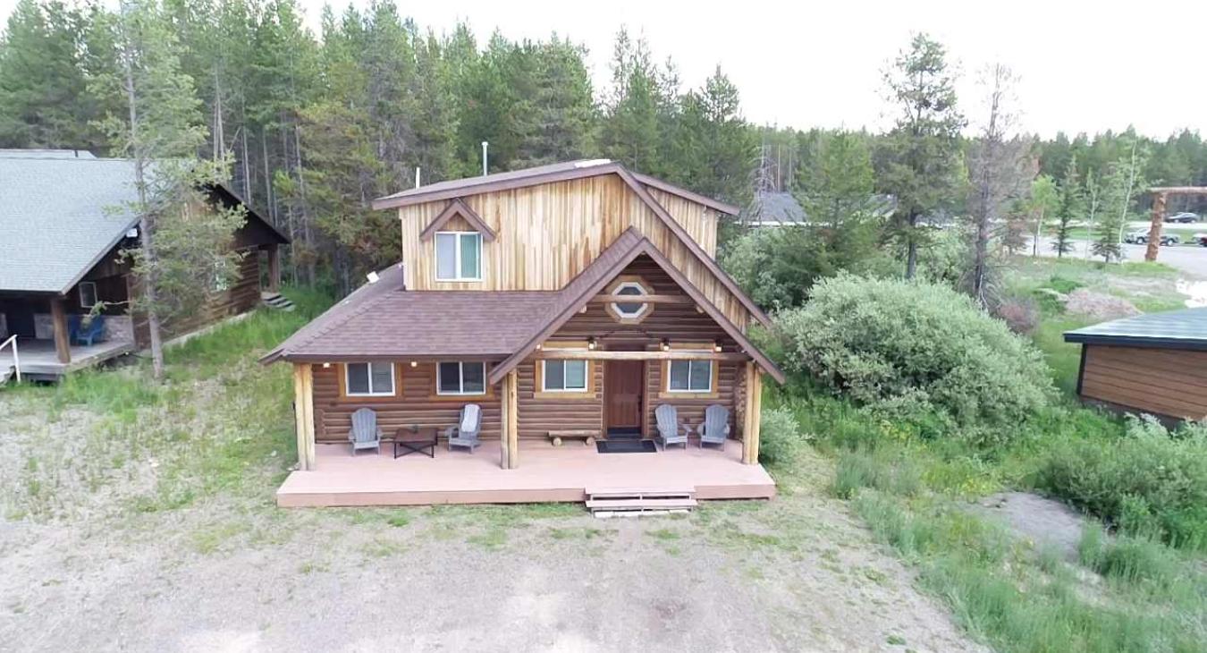 A bird's-eye view highlights the cabin's stunning architecture, expansive front deck, and peaceful location nestled among lush evergreen trees.