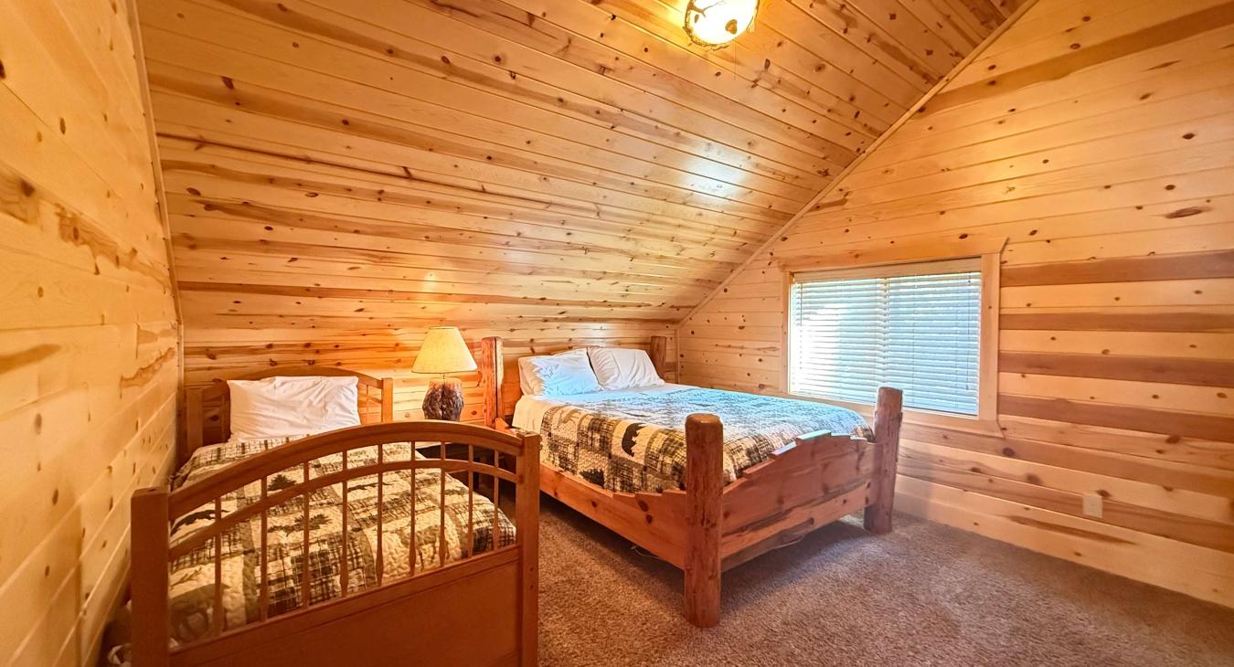The second upstairs bedroom offers flexible sleeping options with a comfortable log Queen bed and a matching single twin bed side-by-side.