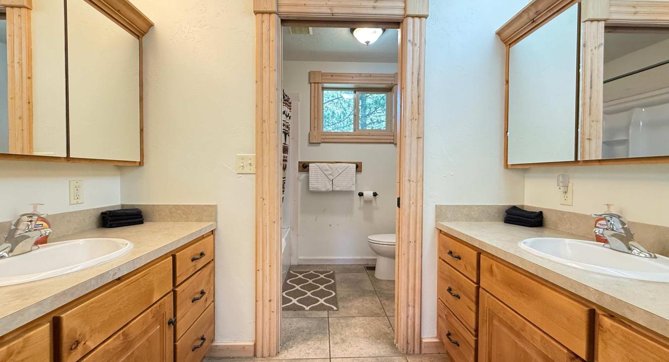 Loft bathroom with 2 vanities and sinks. Door between the sinks and bath/toilet area.
