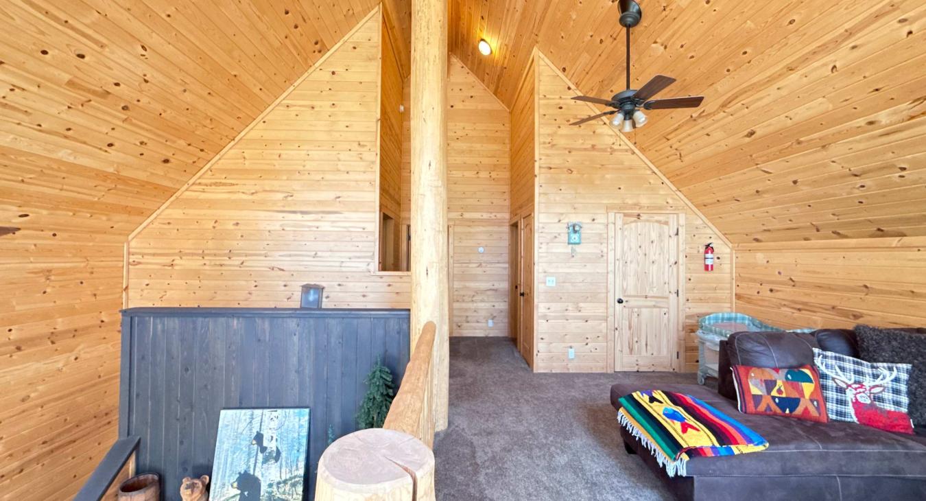 Head upstairs to the expansive open-loft area, showcasing high vaulted ceilings, rich wooden paneling, and a flexible secondary living space for the whole family.