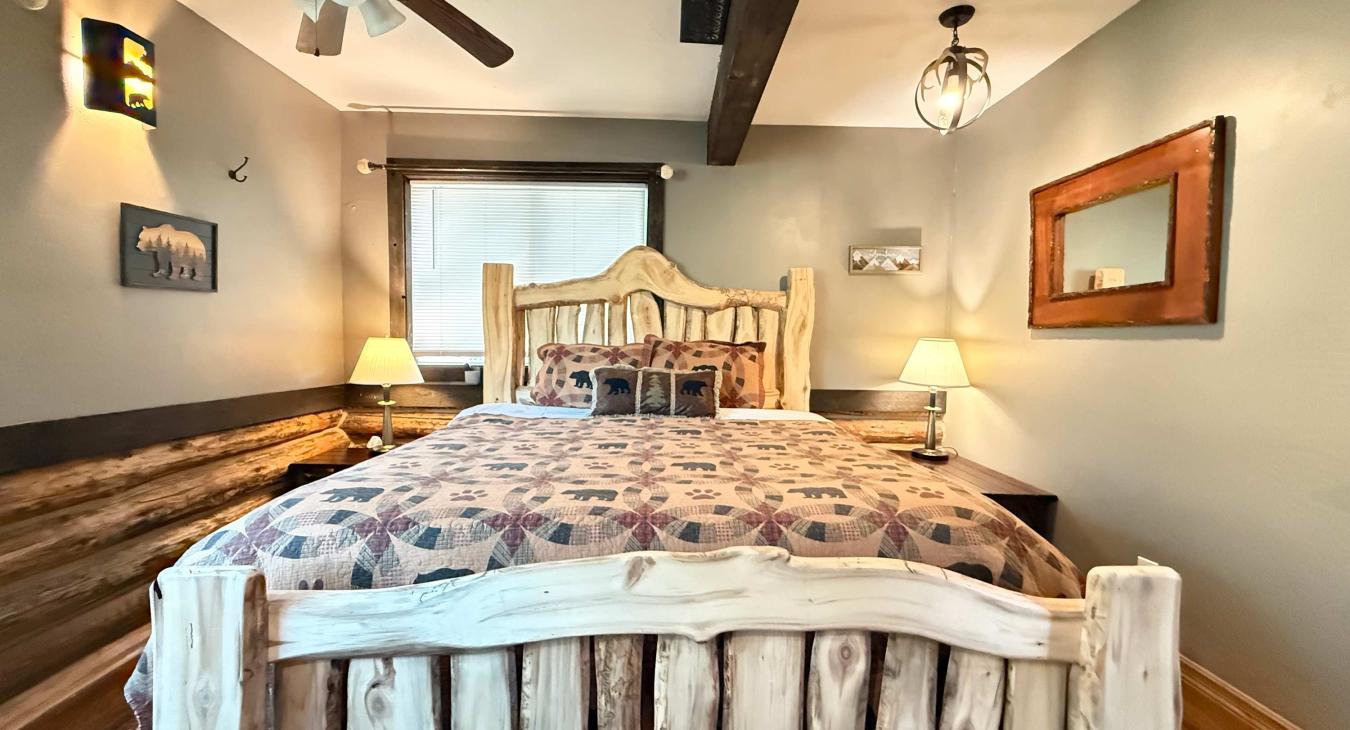 Relax in the grand master bedroom, featuring a stunning rustic log-framed King bed, warm lighting, and beautiful accent wood paneling.