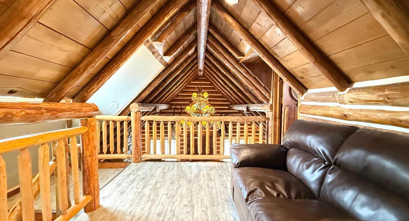 The open upstairs loft area features a comfortable leather sofa nestled under striking log A-frame ceilings, offering a cozy spot to relax.