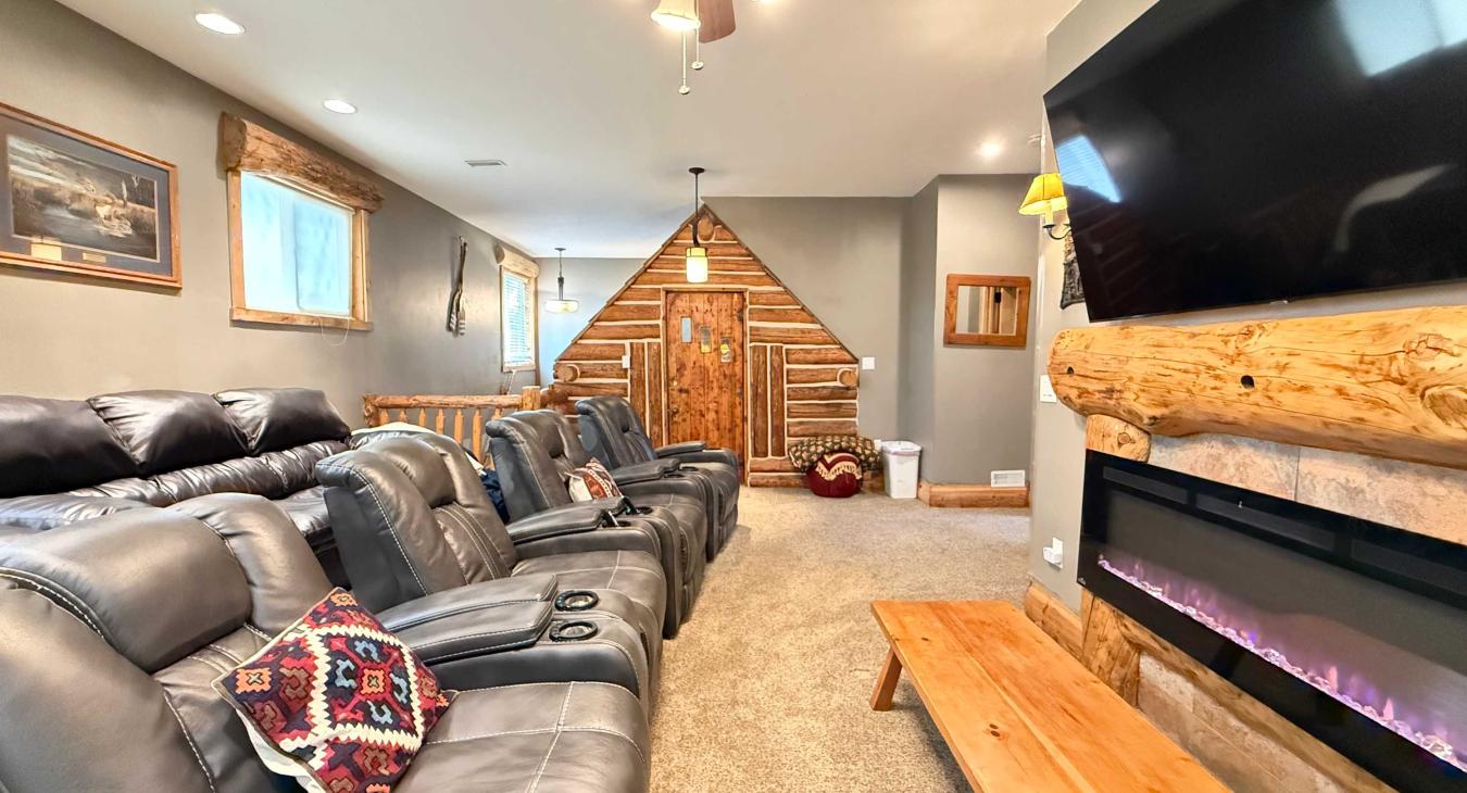 This impressive theater room features multiple plush leather reclining chairs, a large wall-mounted Smart TV, and a cozy electric fireplace.
