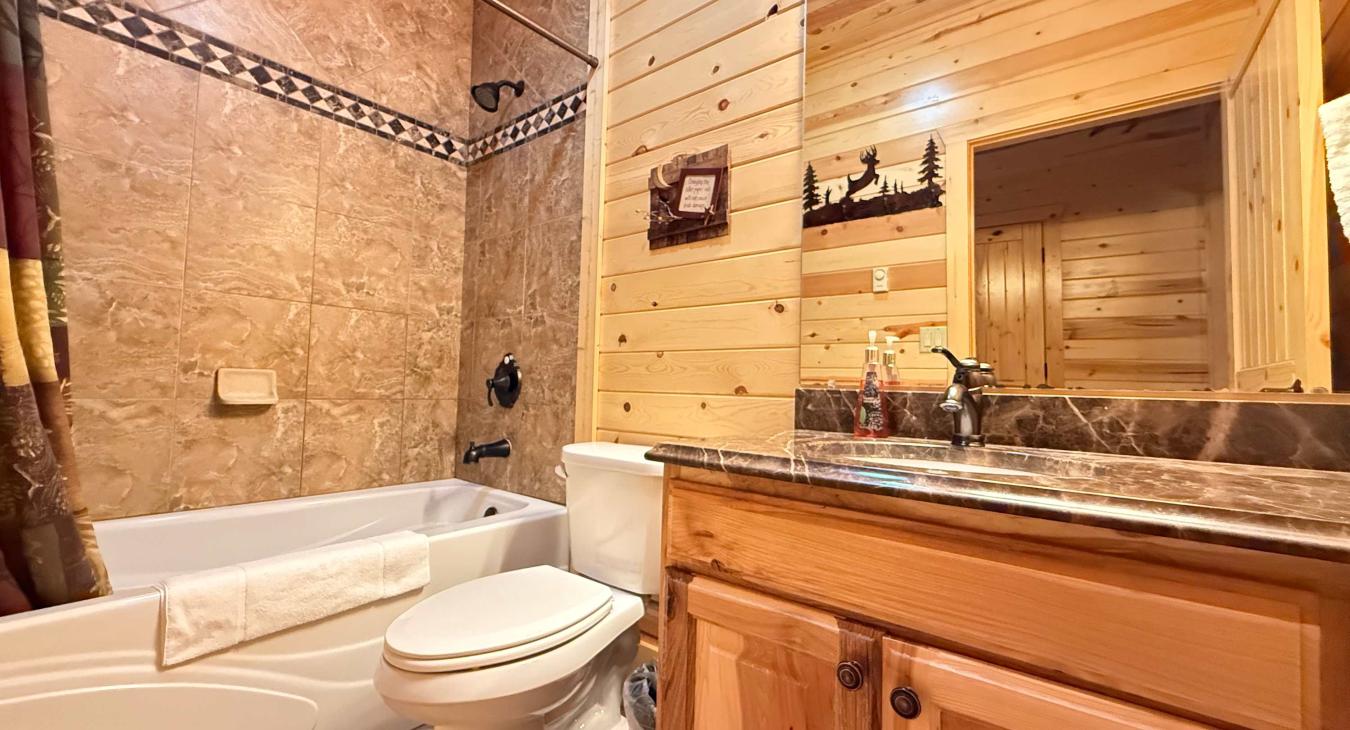 The convenient main-floor shared bathroom offers a beautiful wooden vanity, toilet, and a clean shower-and-tub combo for a relaxing soak.