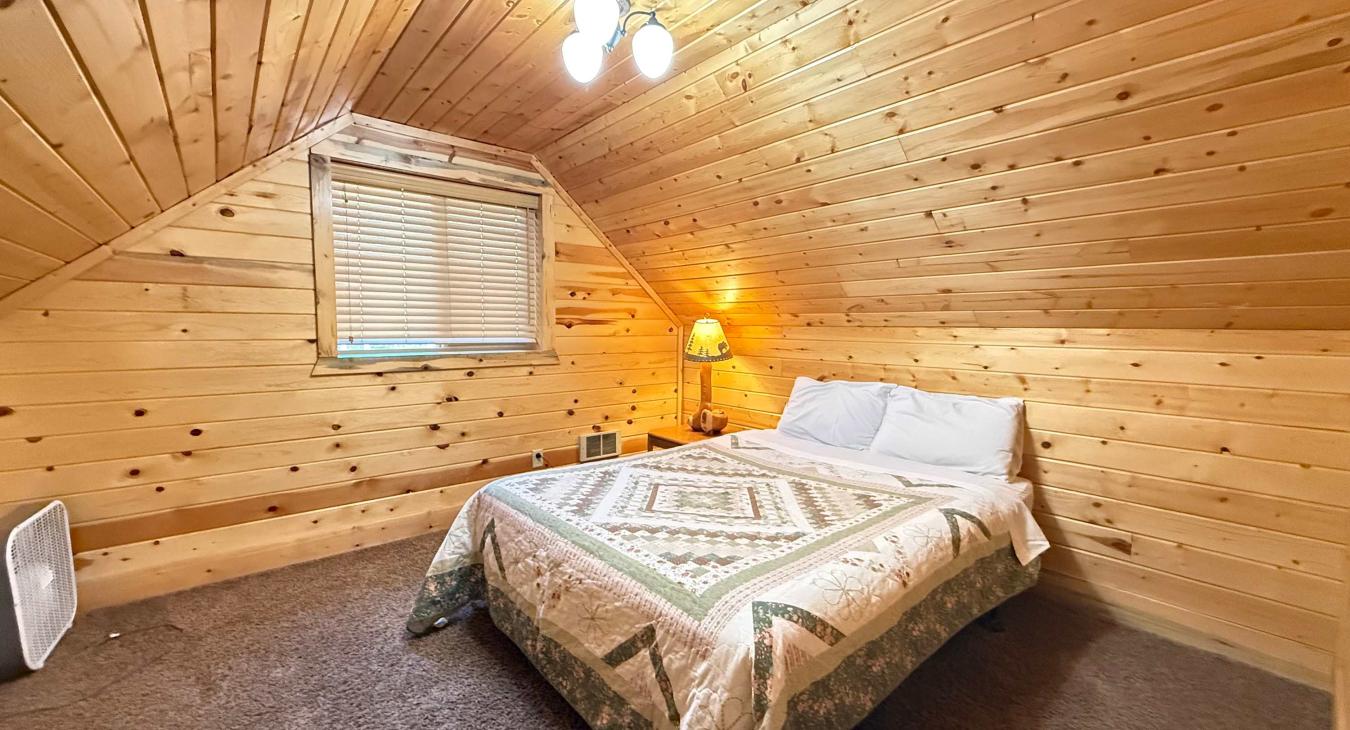 Rest easy in the private garage studio queen bedroom, featuring a comfortable bed under warm wood paneling and bright lighting.