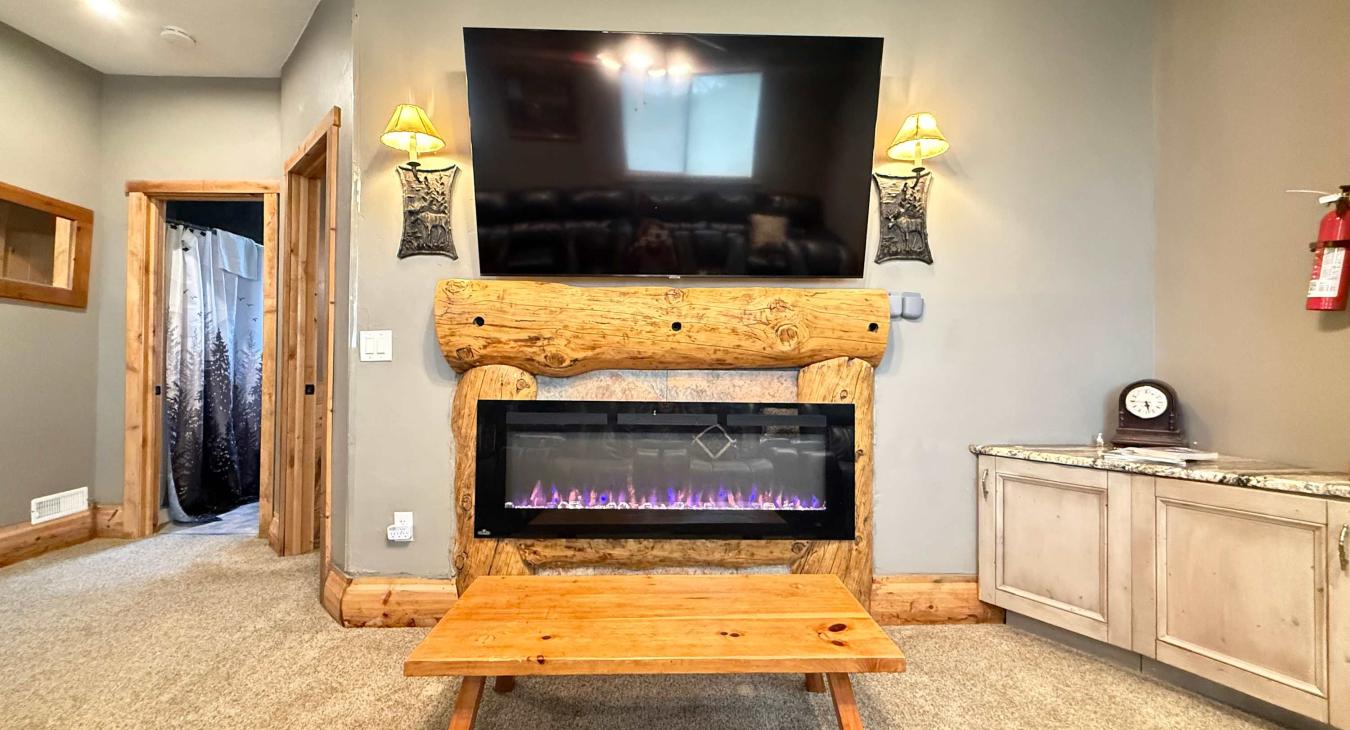 Enjoy a premium movie night experience anchored by a massive log-framed fireplace mantel and a sleek electric fireplace setup.