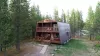 The front of the cabin has a simple, rustic design with lots of wood siding and a small porch. It's also small, with a single entrance. You can also see the surrounding forest from this angle.