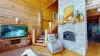 Imagine walking into a cozy yet spacious living room in a cabin, where rustic charm meets comfort. The focal point of the room is a grand stone fireplace, its warm hearth crackling with a soft fire.