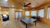 The basement of the cabin has been transformed into a vibrant and cozy game room, offering a perfect retreat for fun and relaxation. Near the far wall, there is a small seating area with a few comfortable chairs and a table.