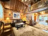 This breathtaking log cabin great room boasts soaring vaulted ceilings, rich wooden beams, and an open layout that leads into the dining space.