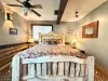 Relax in the grand master bedroom, featuring a stunning rustic log-framed King bed, warm lighting, and beautiful accent wood paneling.