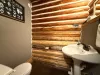 The convenient half bathroom highlights authentic log-cabin craftsmanship, complete with a classic pedestal sink, toilet, and charming forest-themed decor.