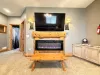 Enjoy a premium movie night experience anchored by a massive log-framed fireplace mantel and a sleek electric fireplace setup.